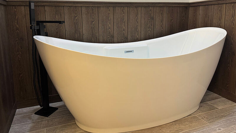 Freestanding white slipper tub with a black floor-mounted tub filler and hand shower, wood-look plank wainscot behind it and wood-look plank flooring beneath