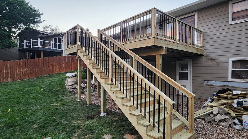 Full stair run from an elevated deck down to grade at dusk, rail and black metal balusters carried down both sides of the flight