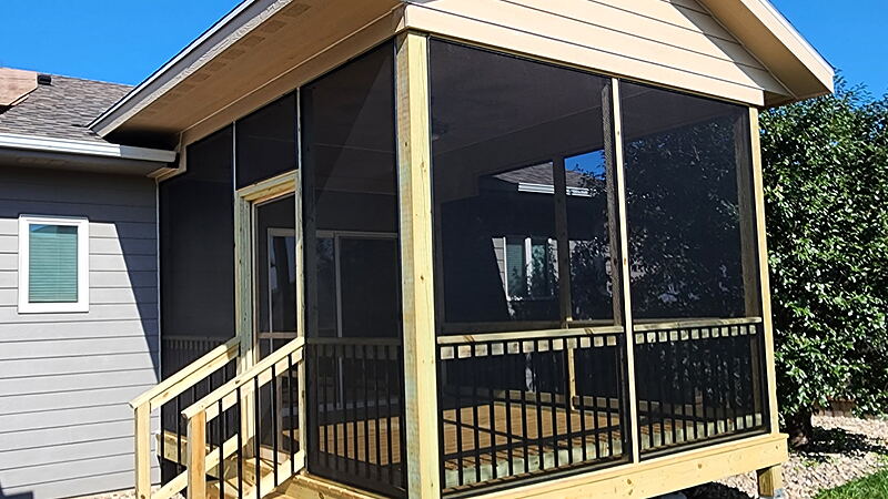 Screened porch addition under its own gable roof, full-height screen panels over a black-baluster half wall, with a screen door and a stair entry