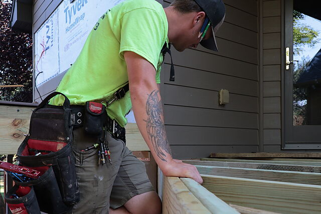 Hols & Co carpenter on a ladder sighting down a new porch beam, one hand checking the line
