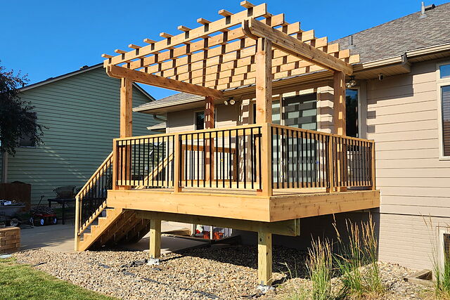 Elevated cedar deck with a lattice-top pergola and black balusters, built off the back of a ranch home