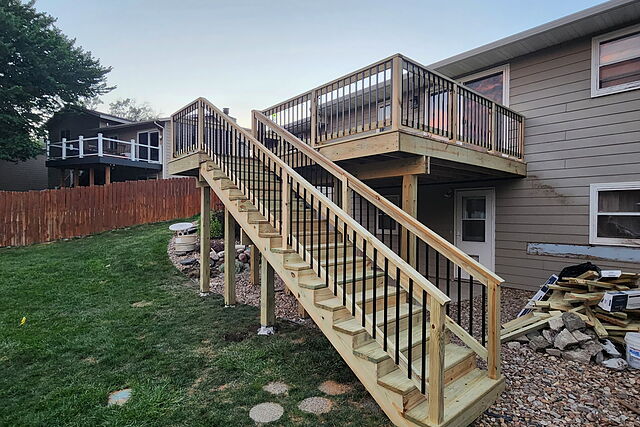 Elevated pressure-treated deck with black metal balusters and a full stair run to grade on the back of a split-level home
