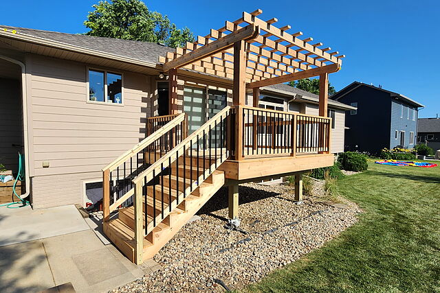 Cedar deck and pergola from the side, showing the stair run to grade and posts set in a rock bed