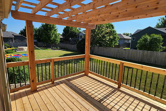 Deck surface under a cedar pergola, looking out over the railing to a fenced back yard