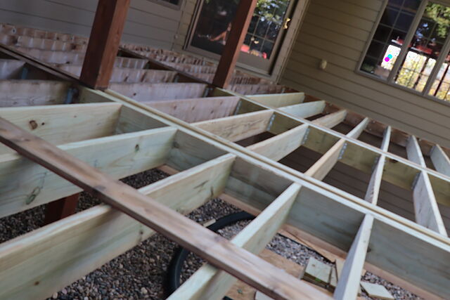 New pressure-treated deck joist framing over river rock, joists set at regular spacing with blocking between them