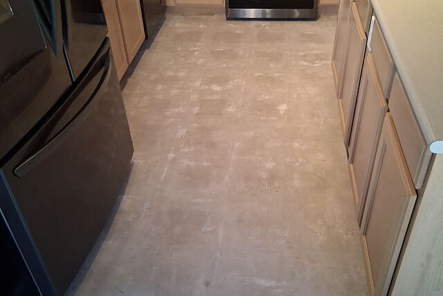 Kitchen with the old flooring removed to bare subfloor between the cabinets and island, appliances still in place