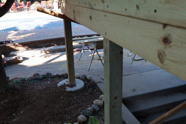 New deck posts bearing on round poured concrete pier footings, fresh rim beam above