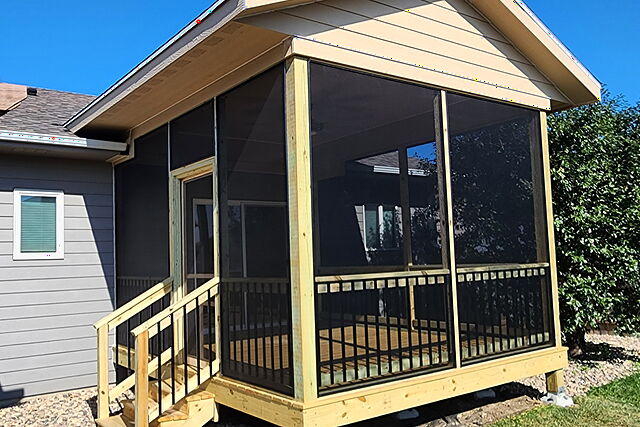 Screened porch addition with its own gable roof, screen walls over a black-baluster half wall, and a stair entry, on the back of a gray ranch home