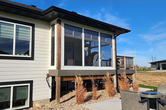 Sunroom with floor-to-ceiling windows and cedar posts over a walkout patio on a white home with black trim, a crew member working inside