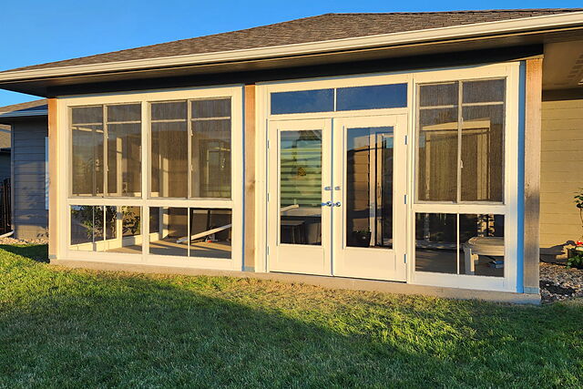 Sunroom enclosure with screened and glass panels and double doors, built on a poured slab against a ranch home